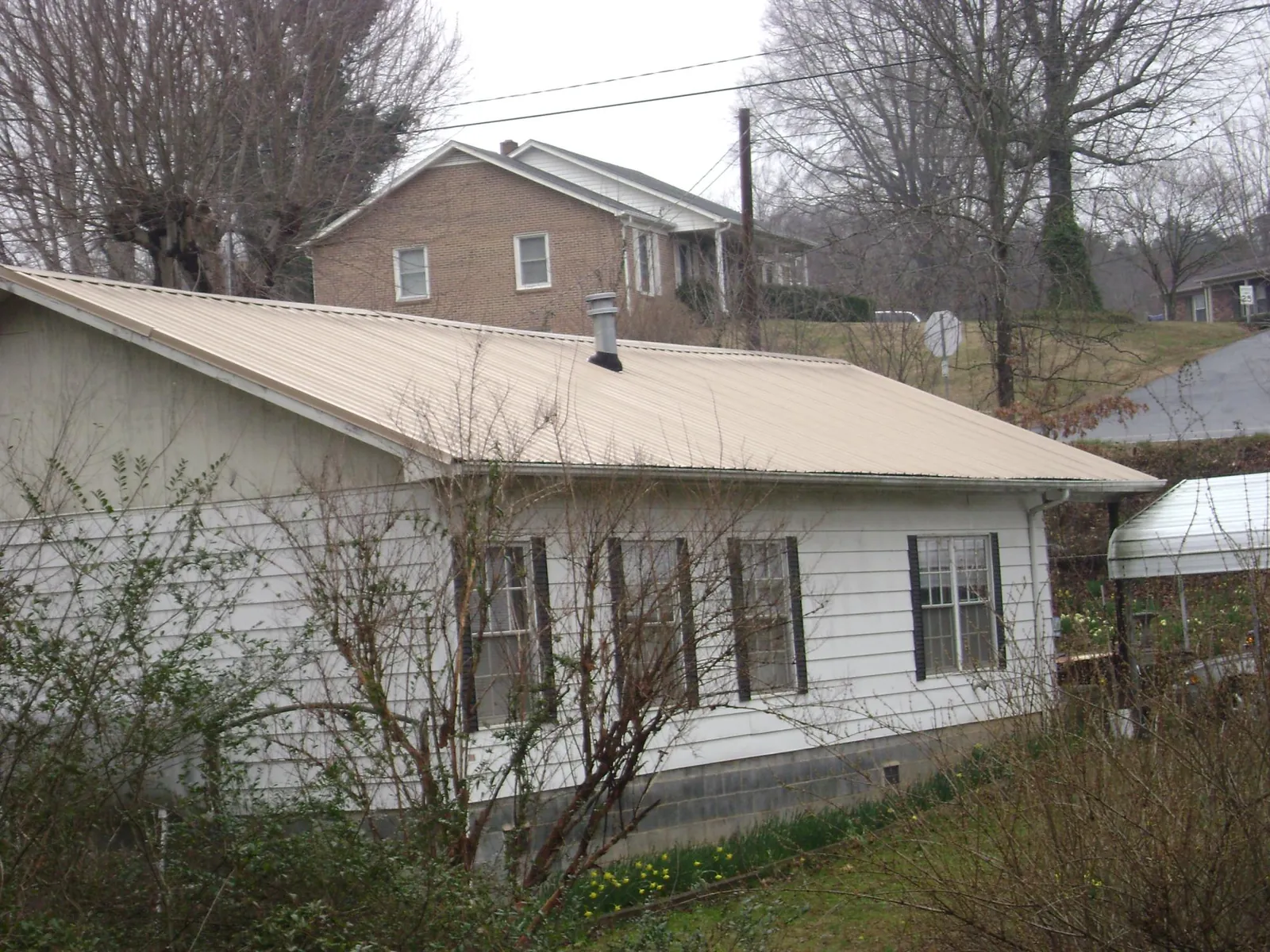 Tan metal roof on a white sided house set into a hillside — Commercial Roofing by Roofing Brothers in Washington